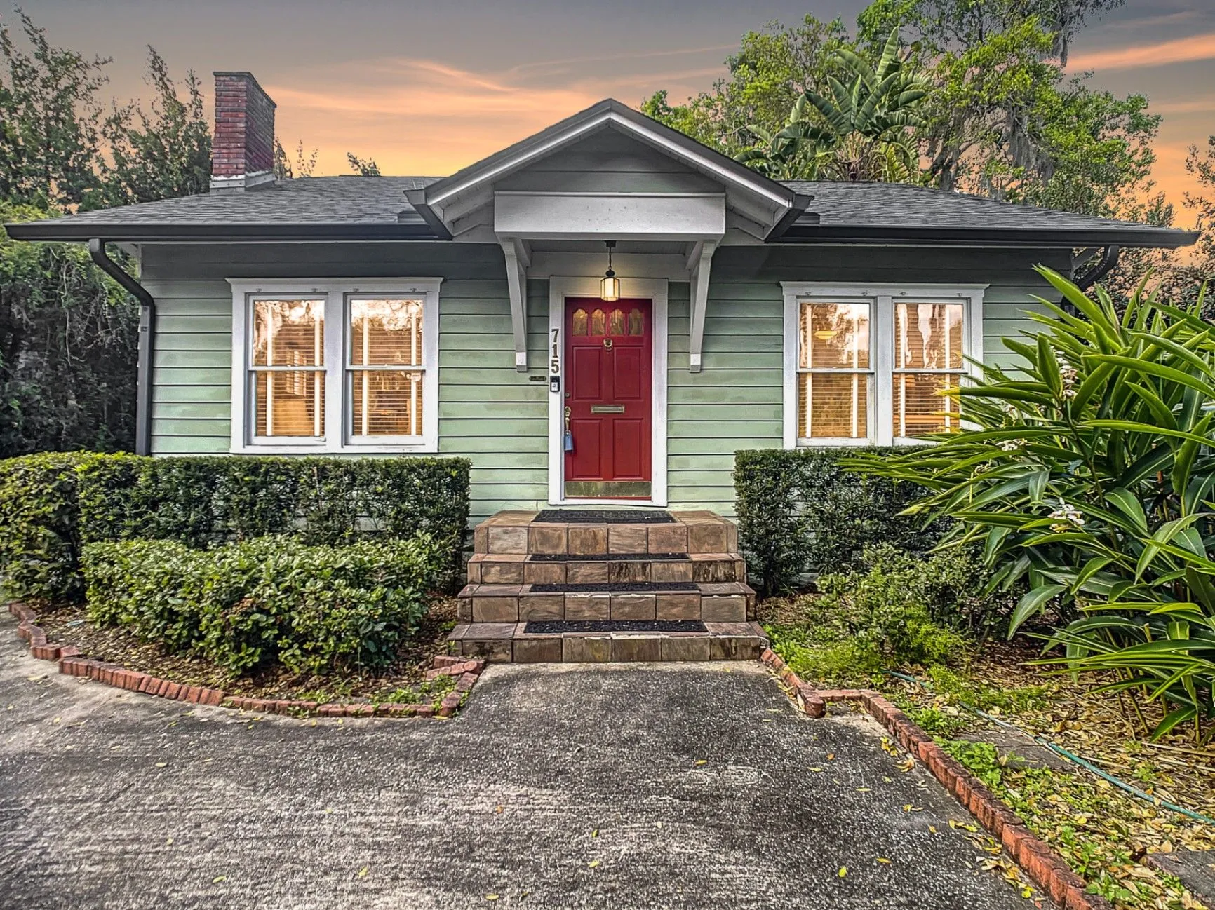 A green bungalow-style home with a landscaped entry